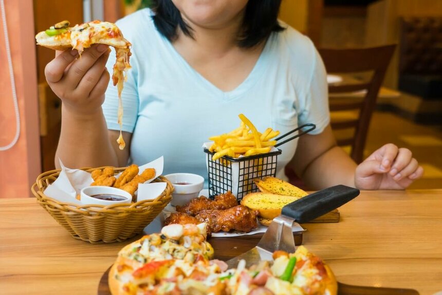 Девушка пришла в кафе и держит в руке пиццу, на столе стоит еда.