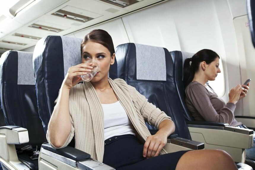 Девушка сидит в кресле самолета и пьет воду.