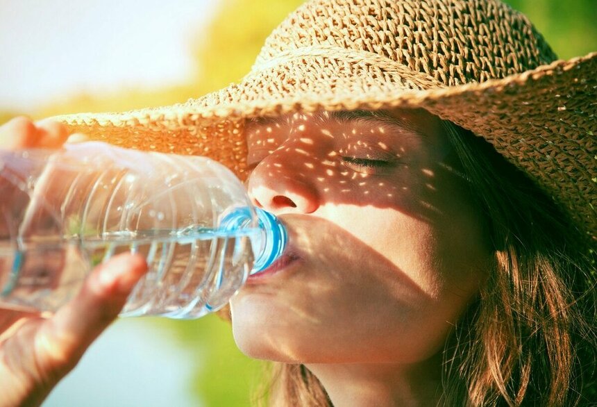 Девушка пьет воду в жаркую погоду.