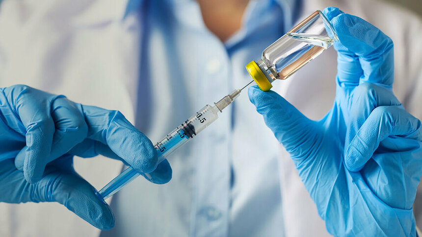 Шприц и ампула с вакциной в руках врача.