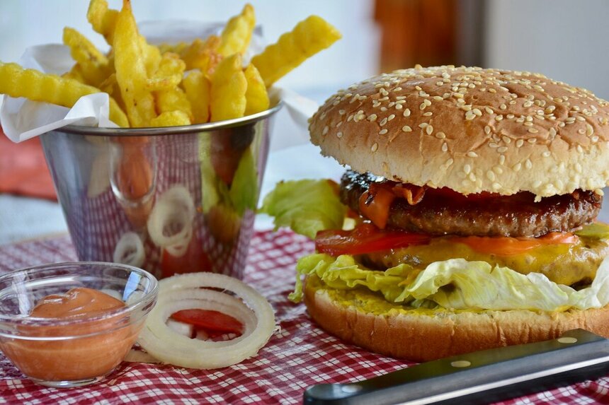 Гамбургер, картошка фри и прочий фастфуд лежат на столе - RitaE