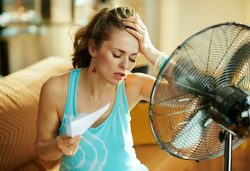 Девушка сидит под вентилятором во время жары.