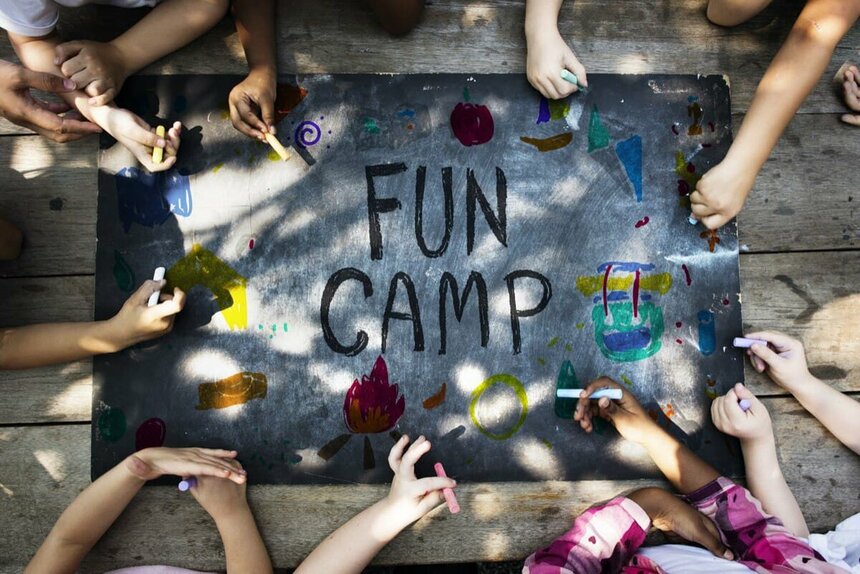 Дети рисуют на доске мелками в летнем лагере.